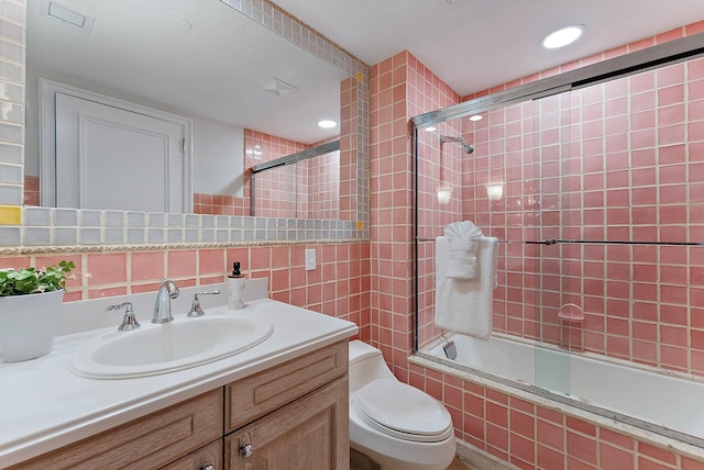 full bathroom with toilet, tasteful backsplash, bath / shower combo with glass door, tile walls, and vanity