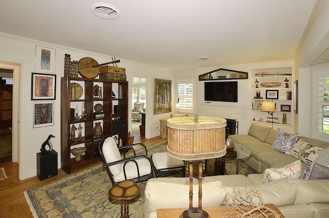 living area with a fireplace, visible vents, wood finished floors, and ornamental molding