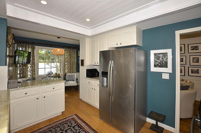 kitchen featuring stainless steel fridge, a raised ceiling, wood finished floors, white cabinetry, and pendant lighting