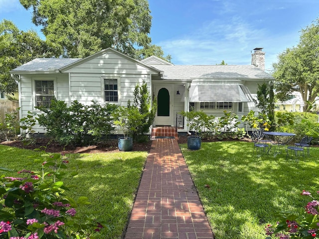 view of front of home featuring a front lawn, a chimney, and a shingled roof