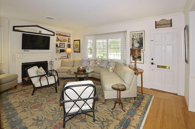 living room with wood finished floors, a fireplace with flush hearth, visible vents, and crown molding