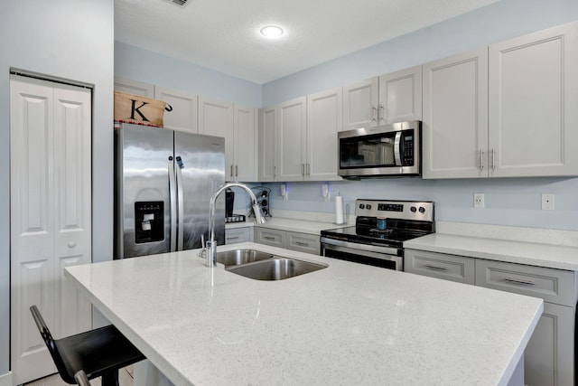 kitchen with sink, a breakfast bar area, stainless steel appliances, light stone countertops, and a kitchen island with sink