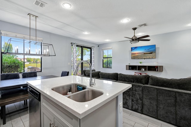 kitchen featuring sink, hanging light fixtures, stainless steel dishwasher, light stone counters, and a center island with sink