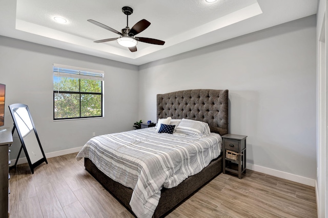 bedroom with a tray ceiling, ceiling fan, and light wood-type flooring