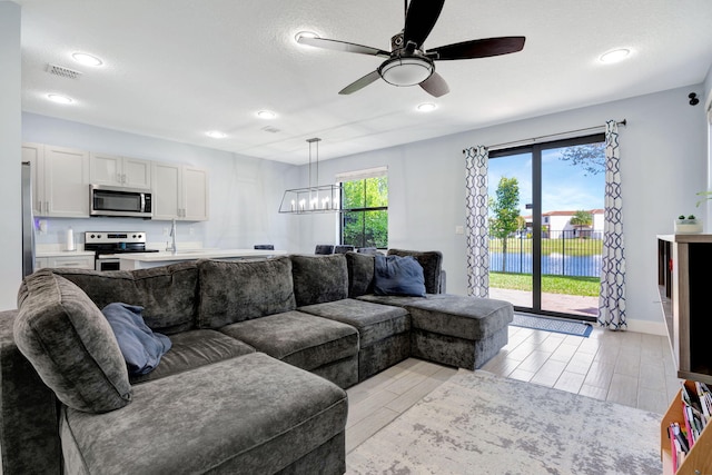 living room with a water view, ceiling fan with notable chandelier, and a textured ceiling