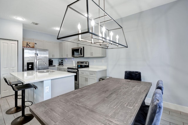 kitchen featuring sink, a breakfast bar area, hanging light fixtures, stainless steel appliances, and a center island with sink