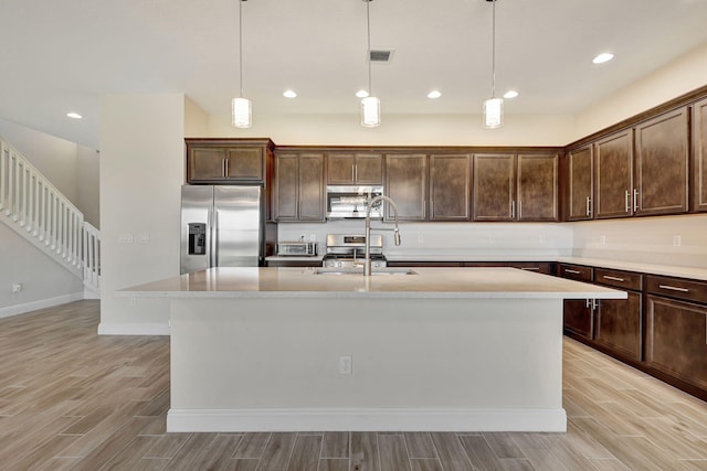 kitchen featuring pendant lighting, sink, stainless steel appliances, dark brown cabinetry, and a center island with sink