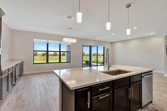 kitchen featuring decorative light fixtures, an island with sink, sink, stainless steel dishwasher, and light hardwood / wood-style flooring