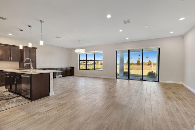 kitchen featuring dark brown cabinetry, sink, decorative light fixtures, light hardwood / wood-style flooring, and an island with sink