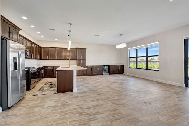 kitchen with a kitchen bar, decorative light fixtures, stainless steel appliances, and a center island with sink