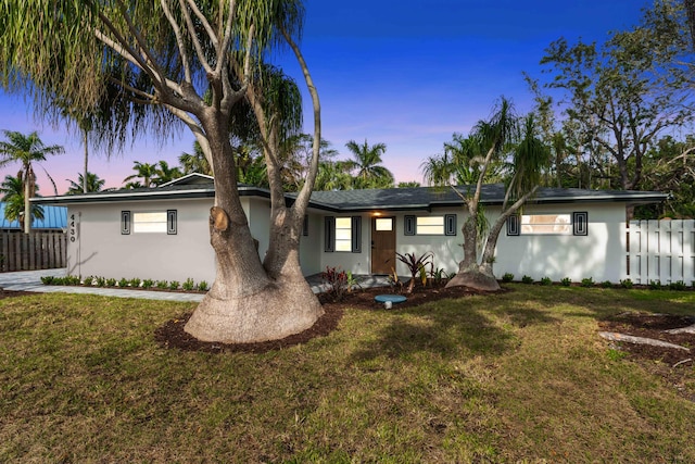 ranch-style home featuring fence, stucco siding, and a front lawn