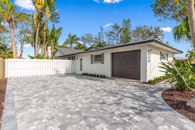 ranch-style home with decorative driveway, a garage, fence, and stucco siding
