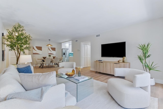 living room with light wood-style floors, visible vents, and baseboards