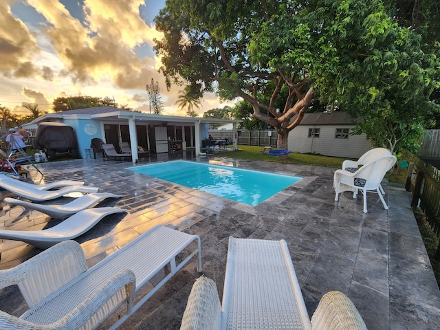 pool at dusk with a patio area and a storage unit