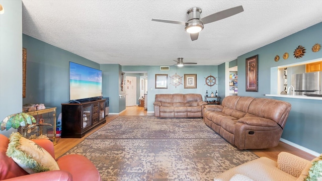 living room featuring ceiling fan, a textured ceiling, and light hardwood / wood-style floors