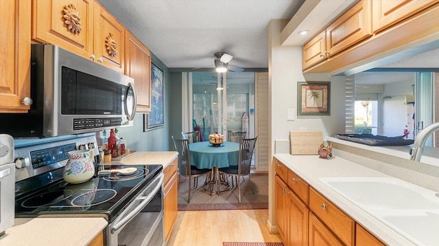 kitchen with stainless steel appliances, ceiling fan, sink, and light hardwood / wood-style floors