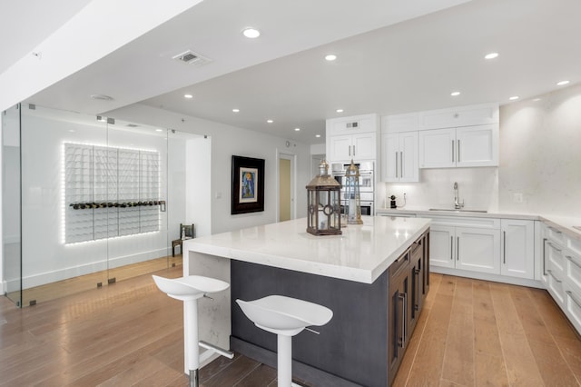 kitchen with white cabinetry, light hardwood / wood-style floors, double oven, and a kitchen island