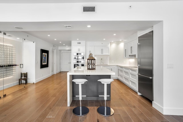 kitchen featuring a breakfast bar area, appliances with stainless steel finishes, white cabinetry, a center island, and wood-type flooring