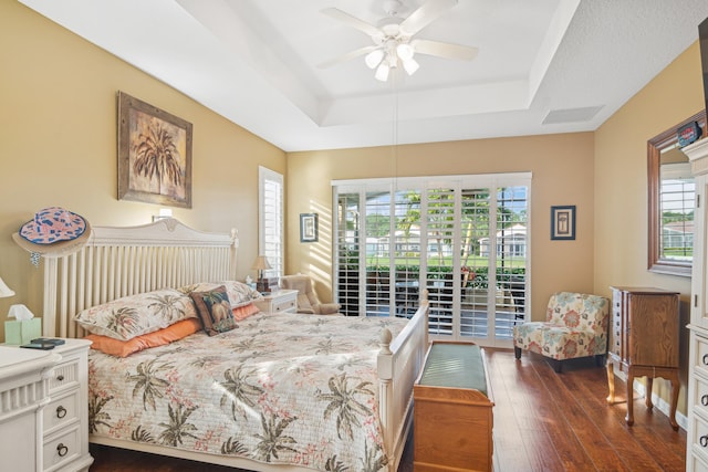 bedroom with dark wood-type flooring, access to outside, ceiling fan, and a tray ceiling