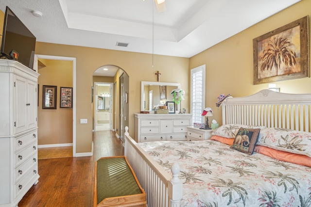 bedroom featuring a raised ceiling, ceiling fan, dark hardwood / wood-style flooring, and ensuite bath