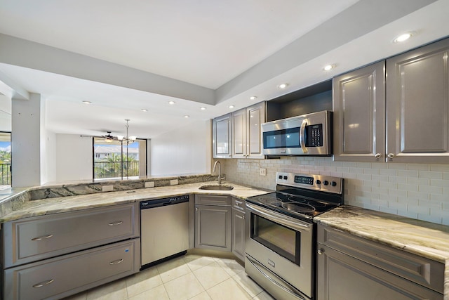 kitchen with sink, appliances with stainless steel finishes, light stone counters, decorative backsplash, and kitchen peninsula