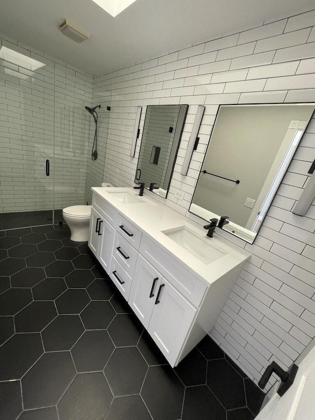 bathroom featuring tile walls, vanity, toilet, a shower with door, and tile patterned floors