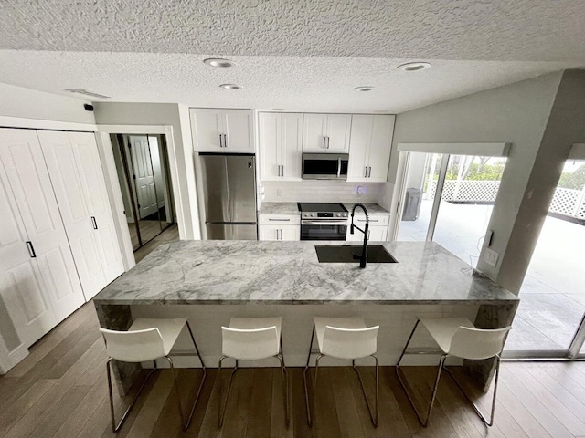 kitchen featuring sink, stainless steel appliances, light stone counters, white cabinets, and a kitchen bar