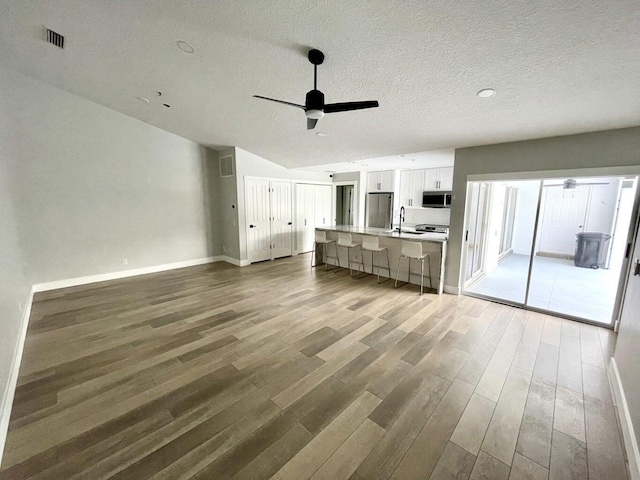 unfurnished living room featuring ceiling fan, wood-type flooring, sink, and a textured ceiling