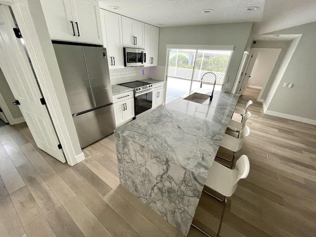 kitchen with stainless steel appliances, white cabinetry, light stone counters, and light hardwood / wood-style floors