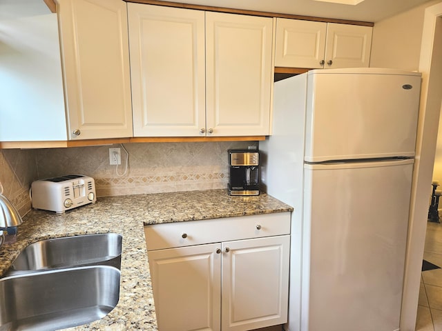 kitchen featuring fridge, sink, white cabinets, and light stone counters