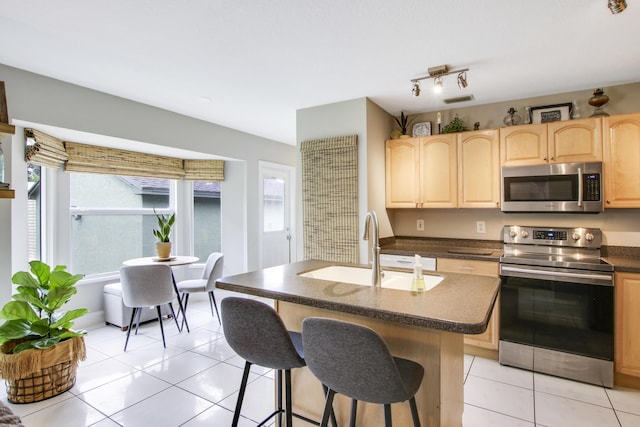 kitchen with light tile patterned flooring, appliances with stainless steel finishes, a breakfast bar, sink, and a kitchen island with sink