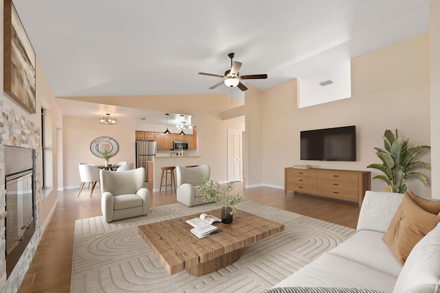 living room featuring ceiling fan, high vaulted ceiling, a fireplace, and light hardwood / wood-style flooring