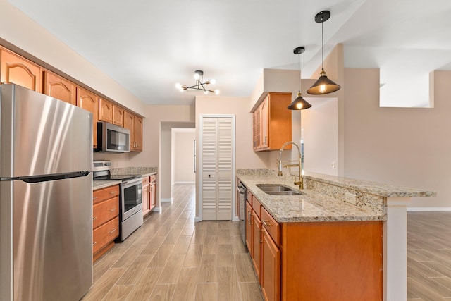 kitchen featuring sink, decorative light fixtures, appliances with stainless steel finishes, kitchen peninsula, and light stone countertops