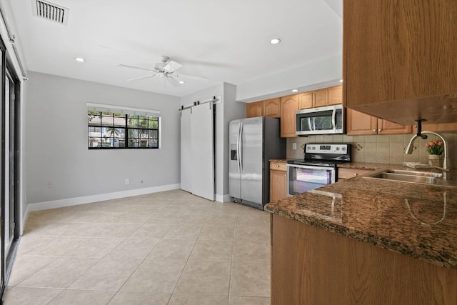 kitchen featuring tasteful backsplash, sink, ceiling fan, stainless steel appliances, and a barn door