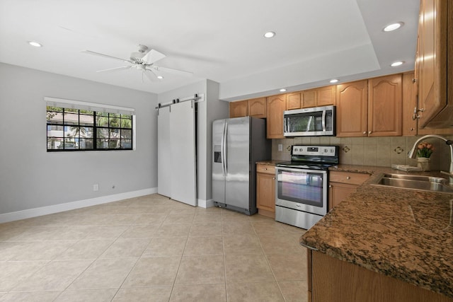 kitchen featuring tasteful backsplash, sink, ceiling fan, stainless steel appliances, and a barn door