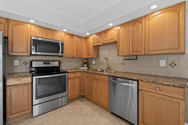 kitchen with sink, light tile patterned floors, appliances with stainless steel finishes, decorative backsplash, and dark stone counters