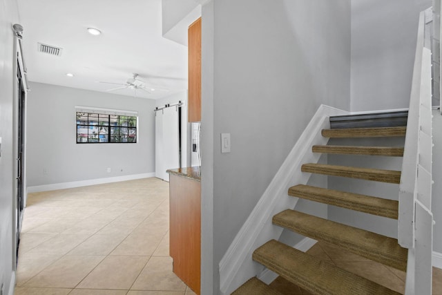 stairs with tile patterned flooring, a barn door, and ceiling fan