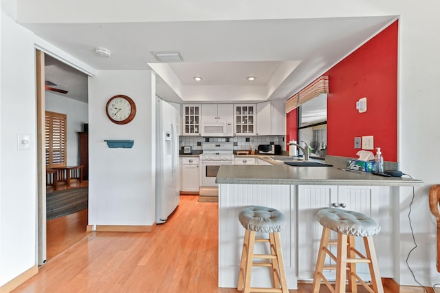 kitchen featuring tasteful backsplash, white cabinets, a kitchen bar, white appliances, and light hardwood / wood-style flooring