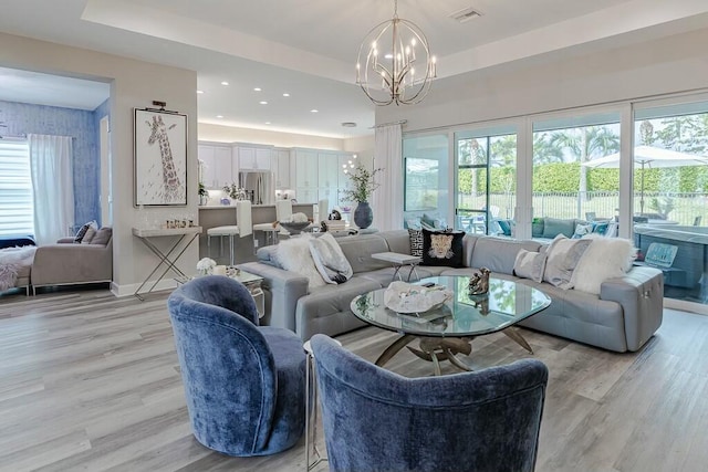 living room featuring a chandelier, light wood finished floors, a raised ceiling, and baseboards