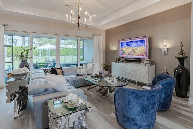 living area with a raised ceiling, visible vents, a wealth of natural light, and a chandelier