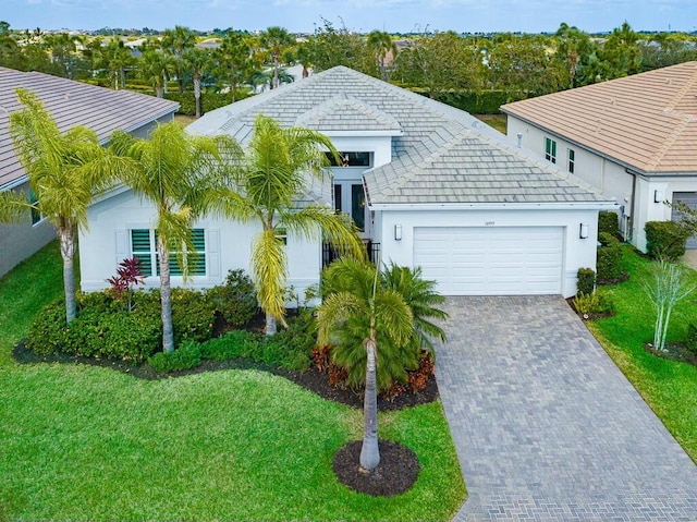 ranch-style home with decorative driveway, an attached garage, stucco siding, and a front yard