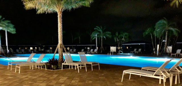 pool at night with a community pool, a patio area, and fence