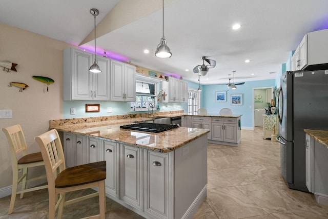 kitchen featuring light stone counters, stainless steel appliances, decorative light fixtures, and kitchen peninsula