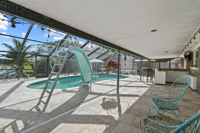 view of swimming pool featuring a water slide, an outdoor bar, glass enclosure, and a patio area