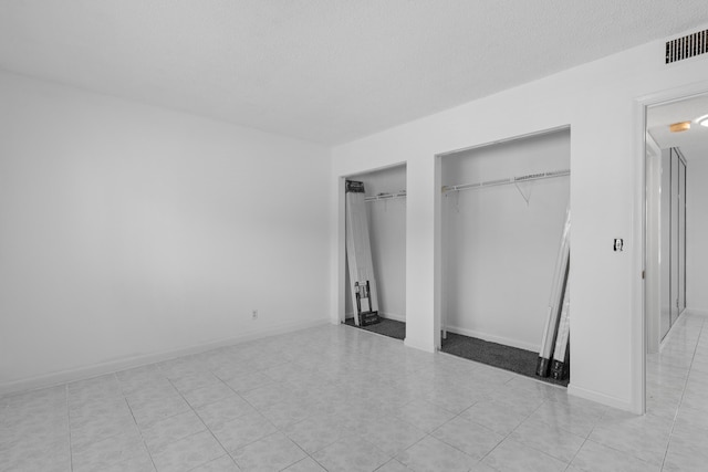 unfurnished bedroom featuring a textured ceiling and multiple closets