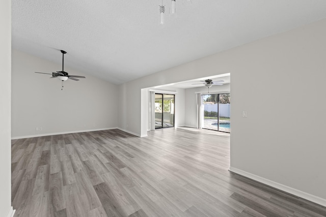 unfurnished living room with vaulted ceiling, ceiling fan, a textured ceiling, and light hardwood / wood-style floors