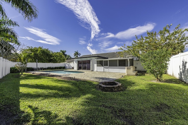 rear view of house with a patio, a fire pit, a yard, a fenced in pool, and a sunroom