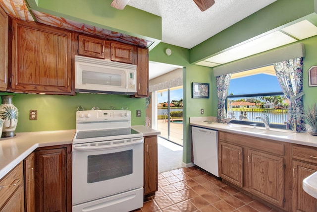 kitchen featuring white appliances, brown cabinetry, a water view, light countertops, and a sink