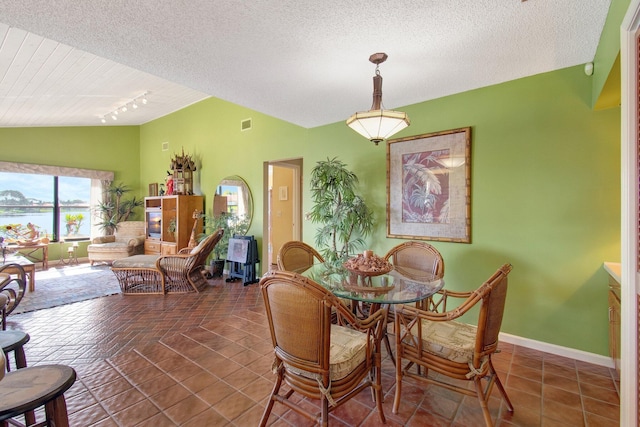 dining area with dark tile patterned floors, vaulted ceiling, track lighting, and a textured ceiling