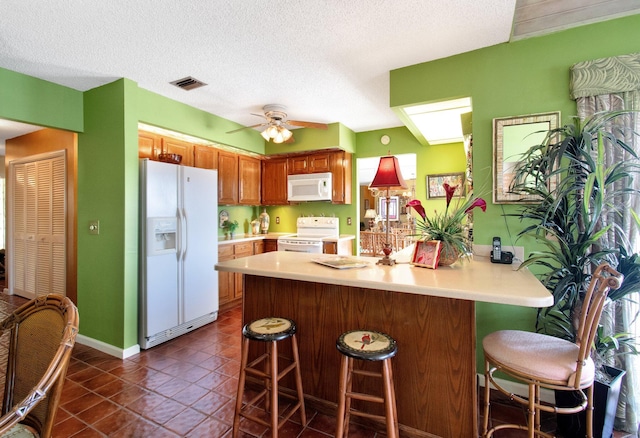 kitchen with white appliances, a breakfast bar, ceiling fan, a textured ceiling, and kitchen peninsula